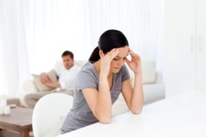 Tired woman having a headache sitting at a table in the lliving room with her boyfriend