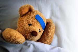 Photo of a sick teddy bear with a blue bandage in bed